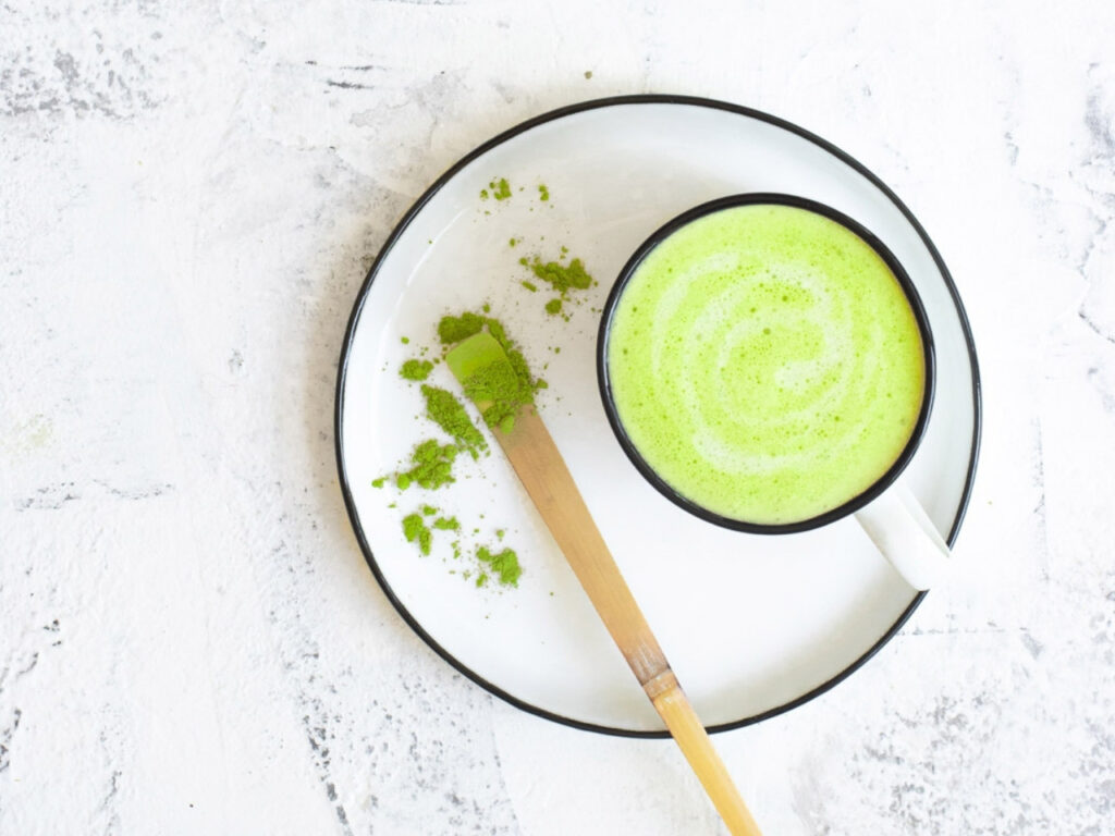 Matcha latte on a white plate with bamboo whisk and matcha powder – a concentrated source of EGCG, known to support metabolism, reduce inflammation and benefit hormone balance in perimenopause.