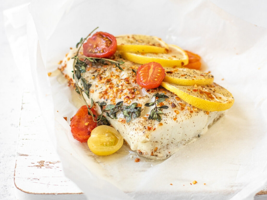 Mediterranean-style cod en papillote (in parchment) with lemon, cherry tomatoes and herbs – a flavourful source of iodine-rich white fish to support thyroid health during perimenopause.