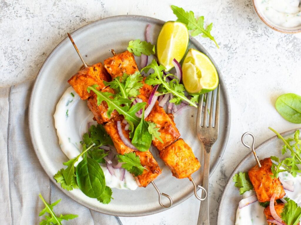 Tandoori salmon skewers served with yoghurt raita and leafy greens – a nutrient-rich meal providing vitamin D, omega-3s and calcium to support bone and hormone health during perimenopause.