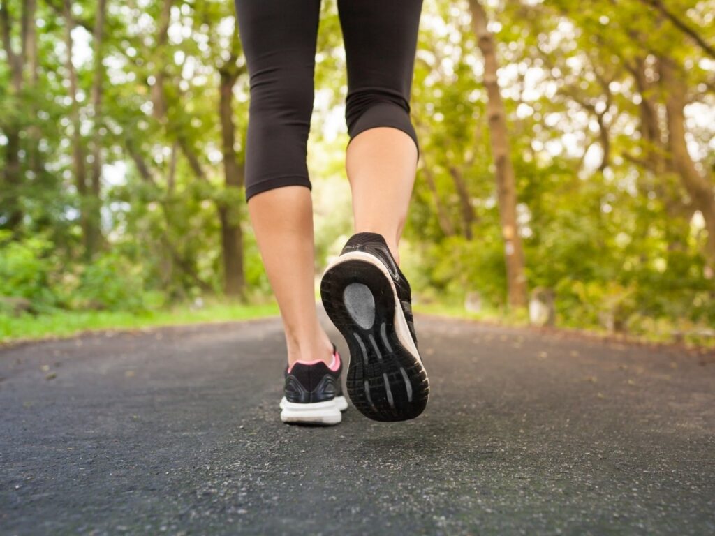 Woman walking outdoors on a tree-lined path – daily walking supports stress reduction, hormone balance and wellbeing during perimenopause.