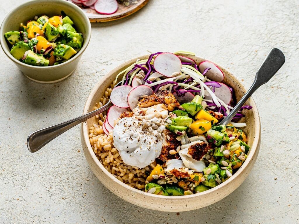 High-protein spicy burrito bowl with white fish, brown rice, avocado mango salsa and colourful vegetables – a nourishing meal to support hormone balance in perimenopause.