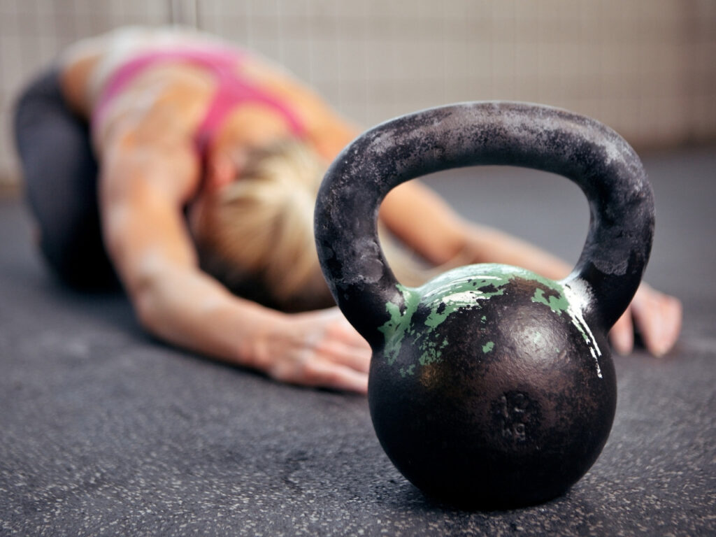 Kettlebell in focus with woman stretching in the background after strength training — supporting recovery and mobility in midlife fitness routines