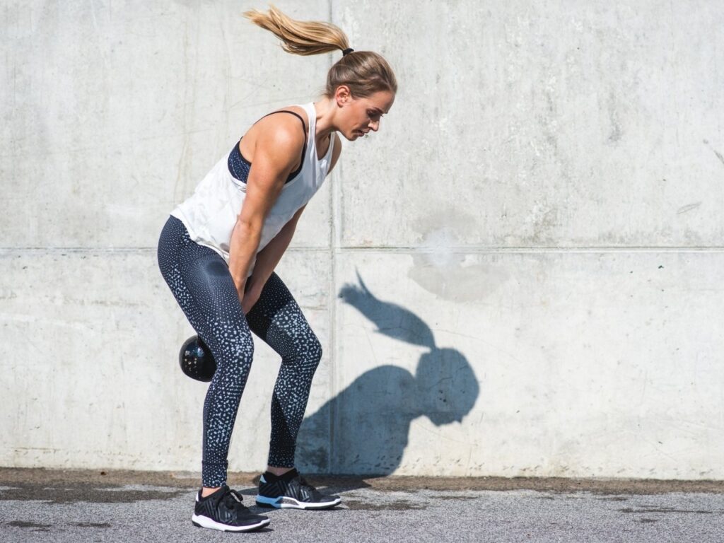 Woman performing kettlebell swing outdoors to build strength and support fat loss during perimenopause.