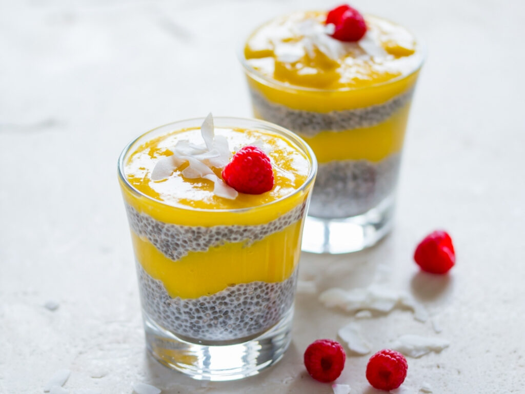 Tropical chia pudding layered with mango purée, topped with coconut flakes and raspberries – a nourishing menopause-friendly breakfast from The Menopause Kitchen.