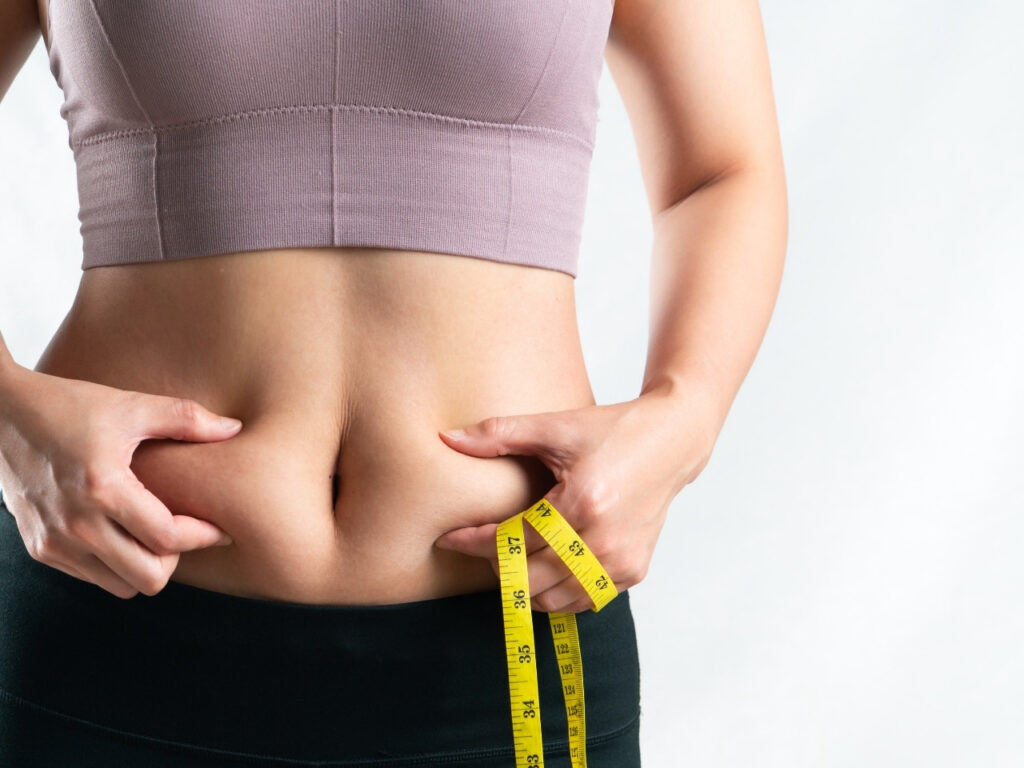 Woman measuring her waist and pinching belly fat — a visual representation of increased abdominal fat and metabolic risk in perimenopause.
